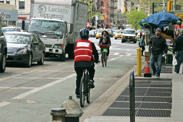 Photo by Sam Spokony A commercial cyclist (foreground, in vest) speeds the wrong way down the Eighth Avenue bike lane, between W. 25th & W. 26th Sts.