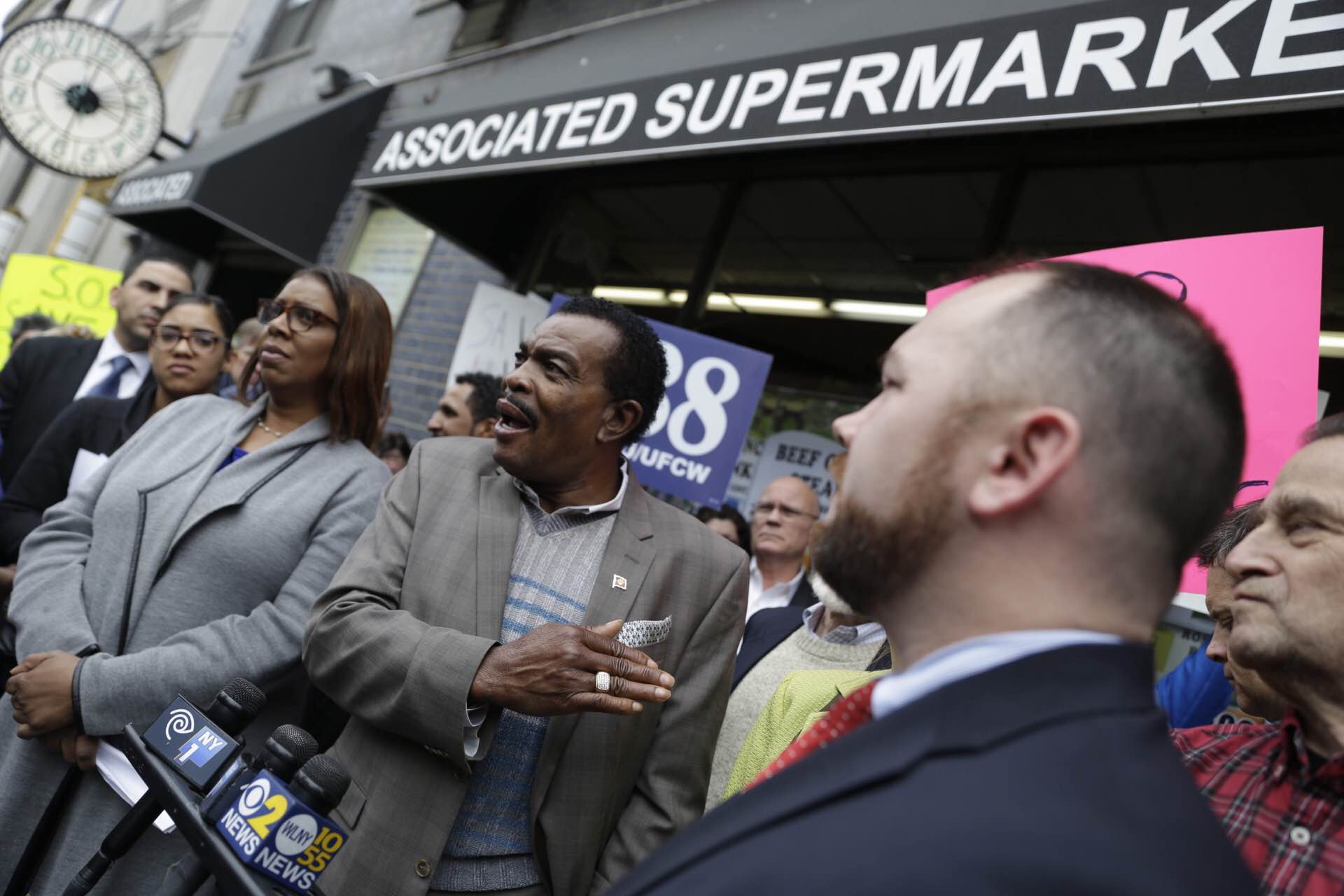 Gladwin Francis, an owner of the W. 14th St. Associated supermarket, spoke at Sunday’s rally, as he was flanked by Councilmember Corey Johnson, right, and Tobi Bergman, C.B. 2 chairperson, right background, and Public Advocate Letitia James, left, and Assemblymember Richard Gottfried, obscured from view behind him.   Photo by William Alatriste / NYC Council