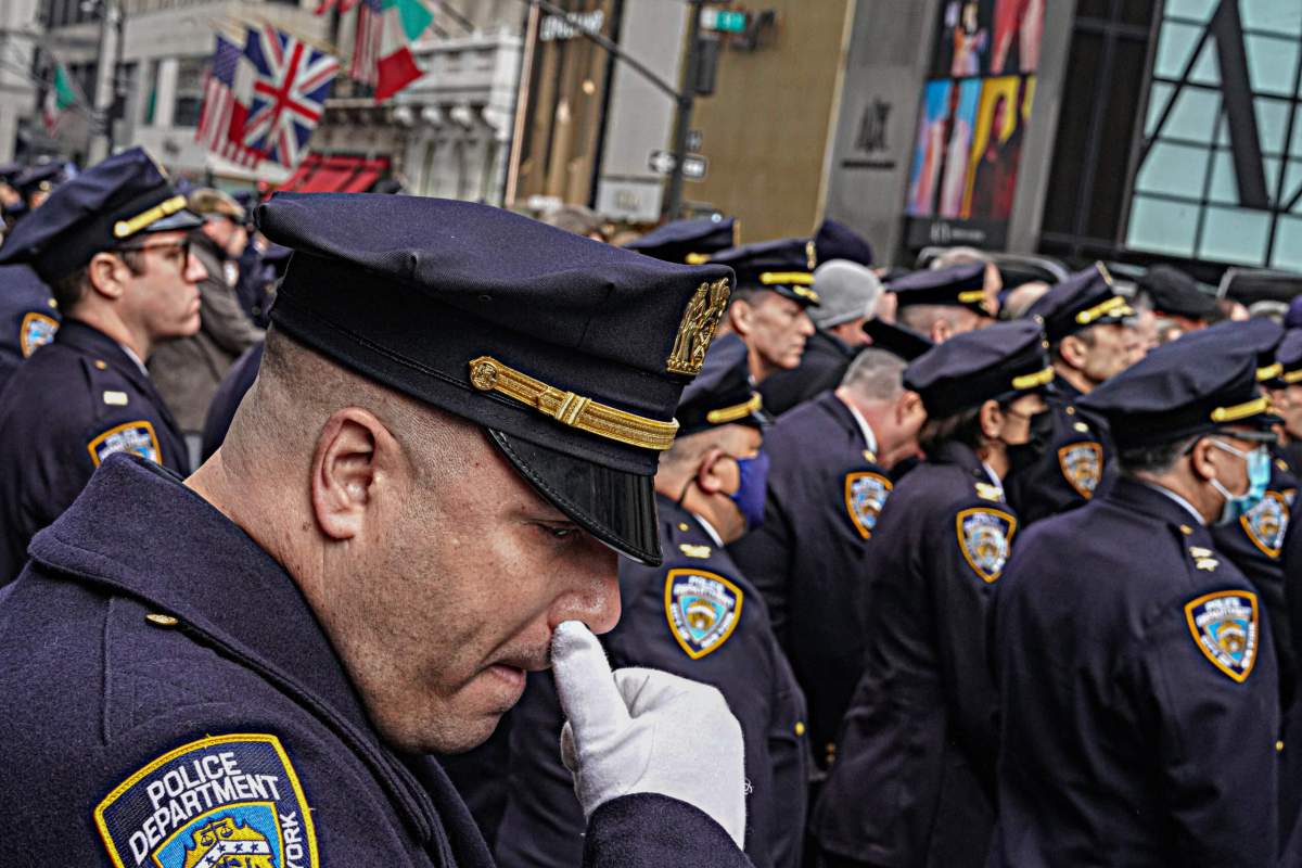 An NYPD officer becomes emotional as Wilbert Mora's coffin is carried out of the cathedral