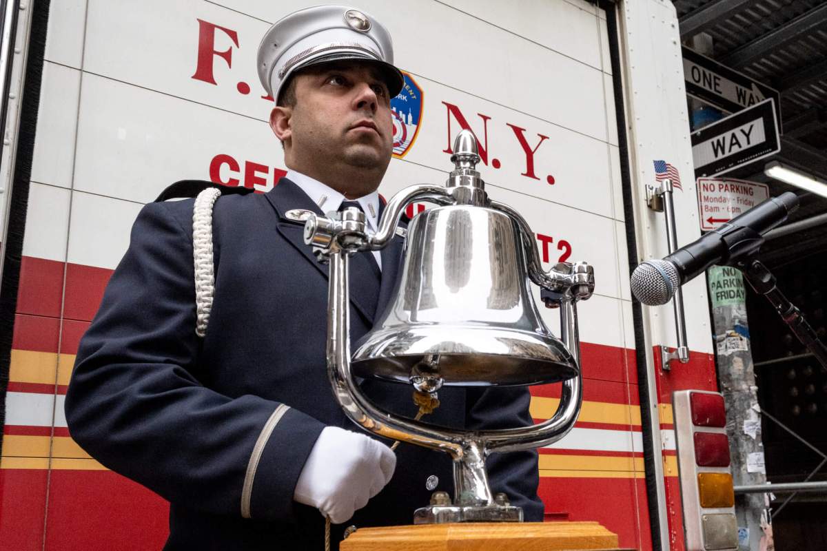 An FDNY firefighter tolls the bell for the victims of the fire. Photo by Gabriele Holtermann