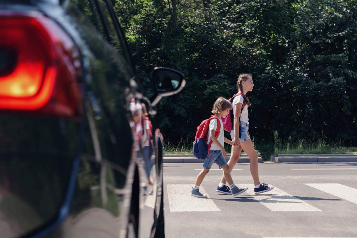 Children next to a car walking through pedestrian crossing to the school