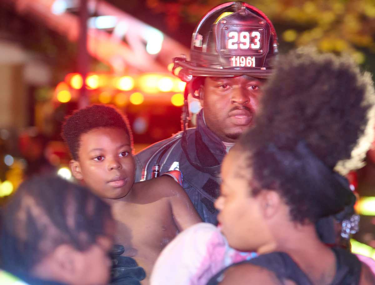 A firefighter from Engine Company 293 helps assist a child from the fire building at 212 Forbell Street.