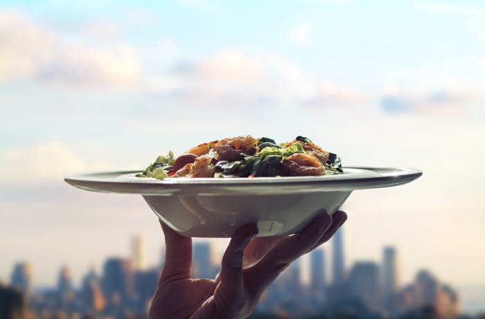 Waitress woman hand with plate of salad on skyscrapers of New York city background. View from roof of restaurant