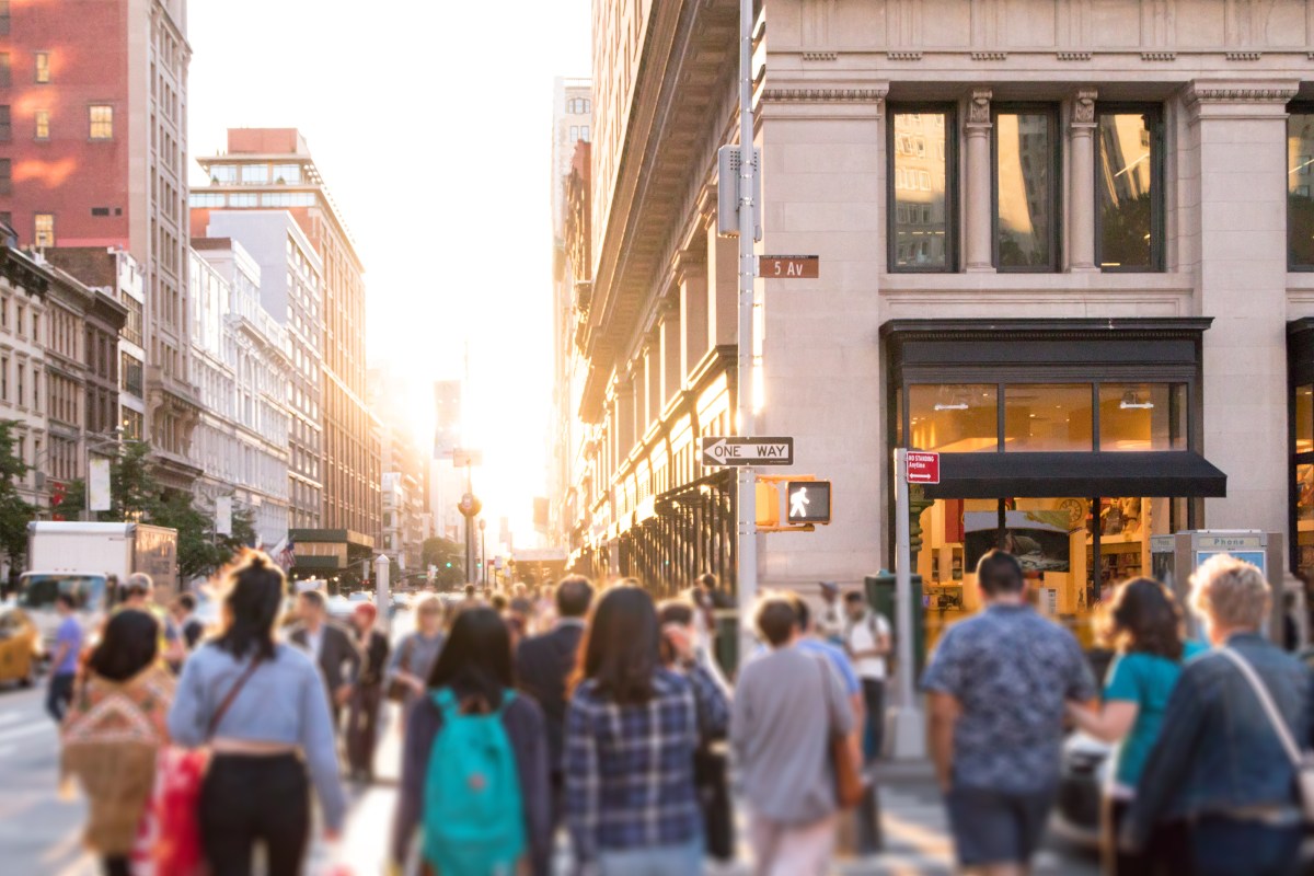 Diverse group of anonymous people walking down busy urban street with bright sunlight shining in the background in New York City