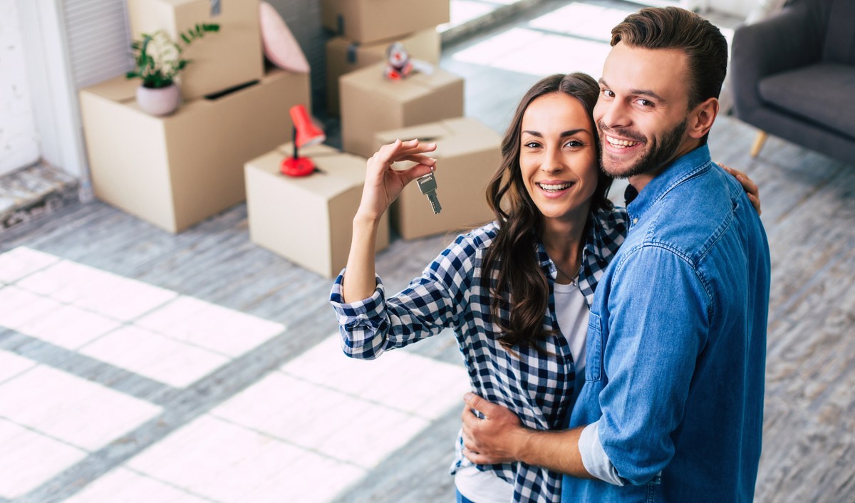 Happy housewarming. A young couple holds happily a key to their new home which they were so excited about, and this can’t but make them feel overwhelmed with positive emotions.