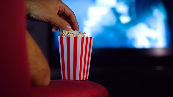 Eating popcorn while watching a movie on the couch at home. Scene in a house with bright lights, a movie night with the scent of pop corn.