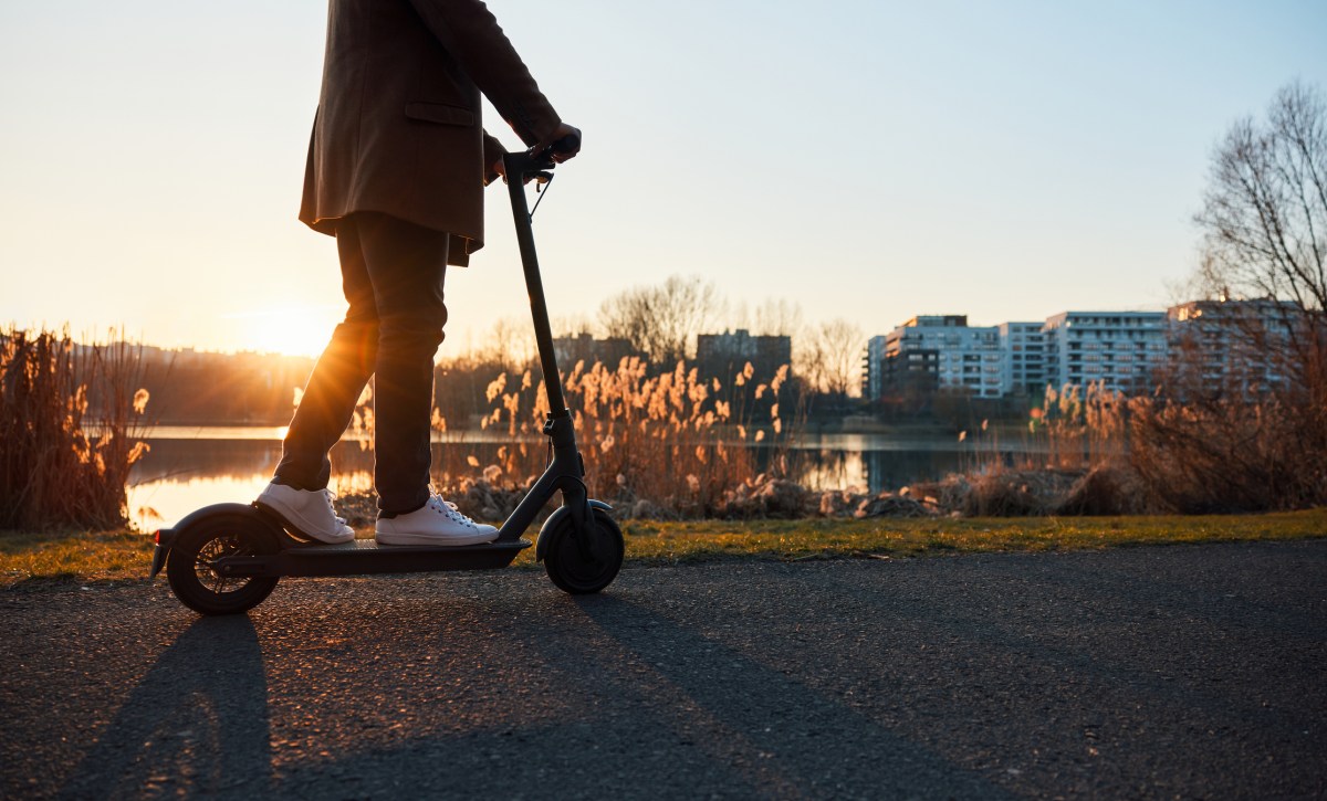 Unrecognisable man riding electric scooter in city during sunset