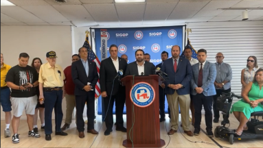 group of men and women inside a building at a podium speaking about attempted assassination of Donald Trump