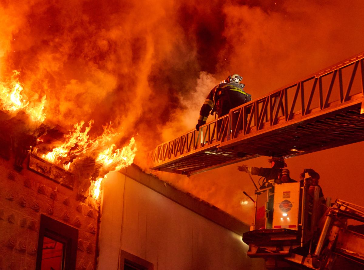 A firefighter retreats from the roof position as heavy fire vents through the roof of a private dwelling during a four alarm fire at 2411 Dean Street.