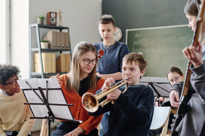 Young Caucasian female music teacher working with middle school orchestra helping boy to practice trumpet