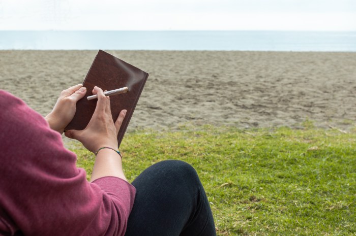 Person reading a book on beach take a break to smoke a marijuana joint or cigarette. Blur background with copy space right.