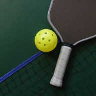 Top view of a pickleball racquet and yellow ball in a green background with a grid