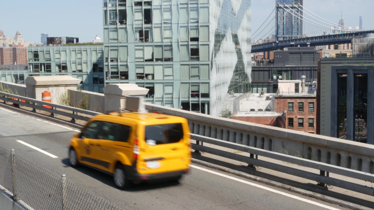 A yellow NYC taxi van crosses the Brooklyn Bridge.