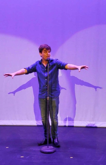 man in blue shirt at a microphone on stage