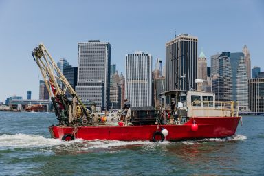 boat preparing to install oysters into NYC waters with city skyline in background