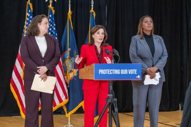 three people at a podium discussing misinformation during Election Day with flags in the back