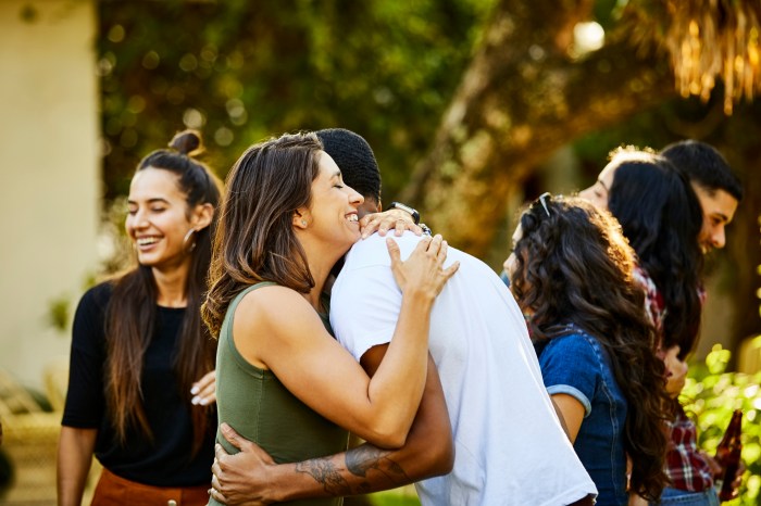 Happy woman embracing friend in backyard during a visit. Male and female hipsters enjoying weekend together. They are wearing casuals.