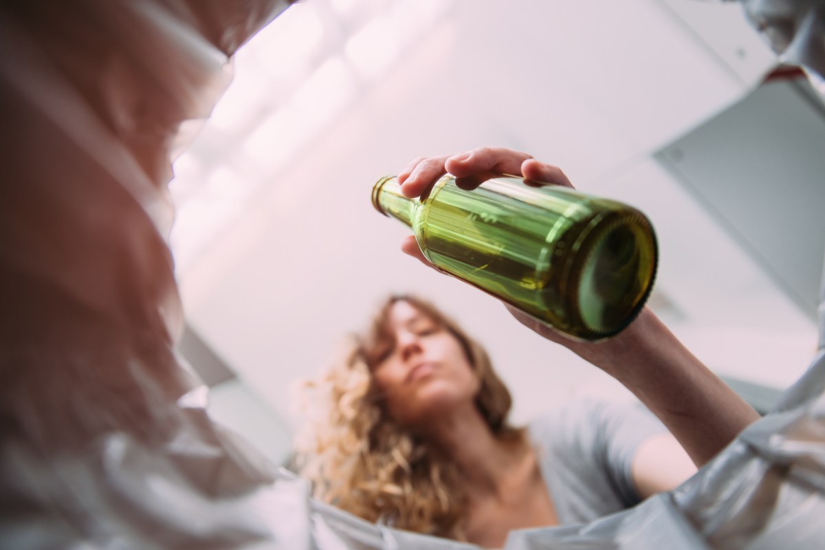 Low angle view of woman throwing beer bottle into glass recycling bin at home