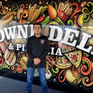 man in a black shirt standing in front of Towne Deli & Pizzeria sign on Staten Island