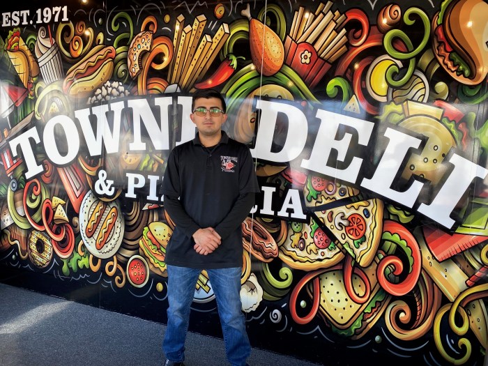 man in a black shirt standing in front of Towne Deli & Pizzeria sign on Staten Island