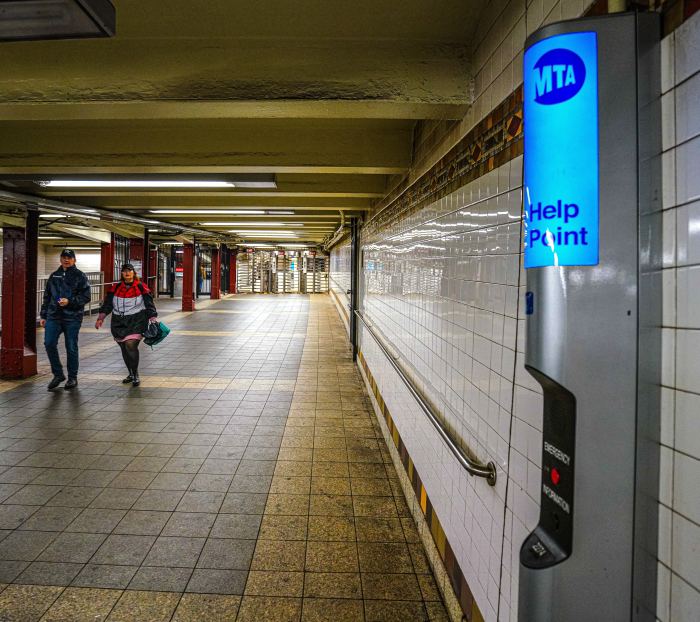 People walking in a subway station next to a NYC subway intercom system kiosk