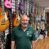 man in front of a row of guitars on a wall inside Castellano's House of Music, a music store in NYC