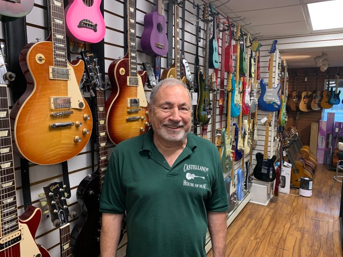 man in front of a row of guitars on a wall inside Castellano's House of Music, a music store in NYC