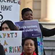 A woman holding a sign reading "Single survivors need shelter too."