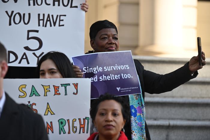 A woman holding a sign reading "Single survivors need shelter too."