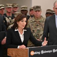 people at a podium during press conference about National Guard troops in NYC subways