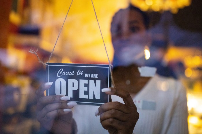 Woman turning an open sign on glass front door of coffee shop. Business owner hanging an open sign at a cafe.