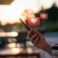 Close up of young woman checking social media network on smartphone on the go in the city. Mobile phone with heart emoji speech bubble message on the screen. People engaging in networking with technology. Social media addiction concept