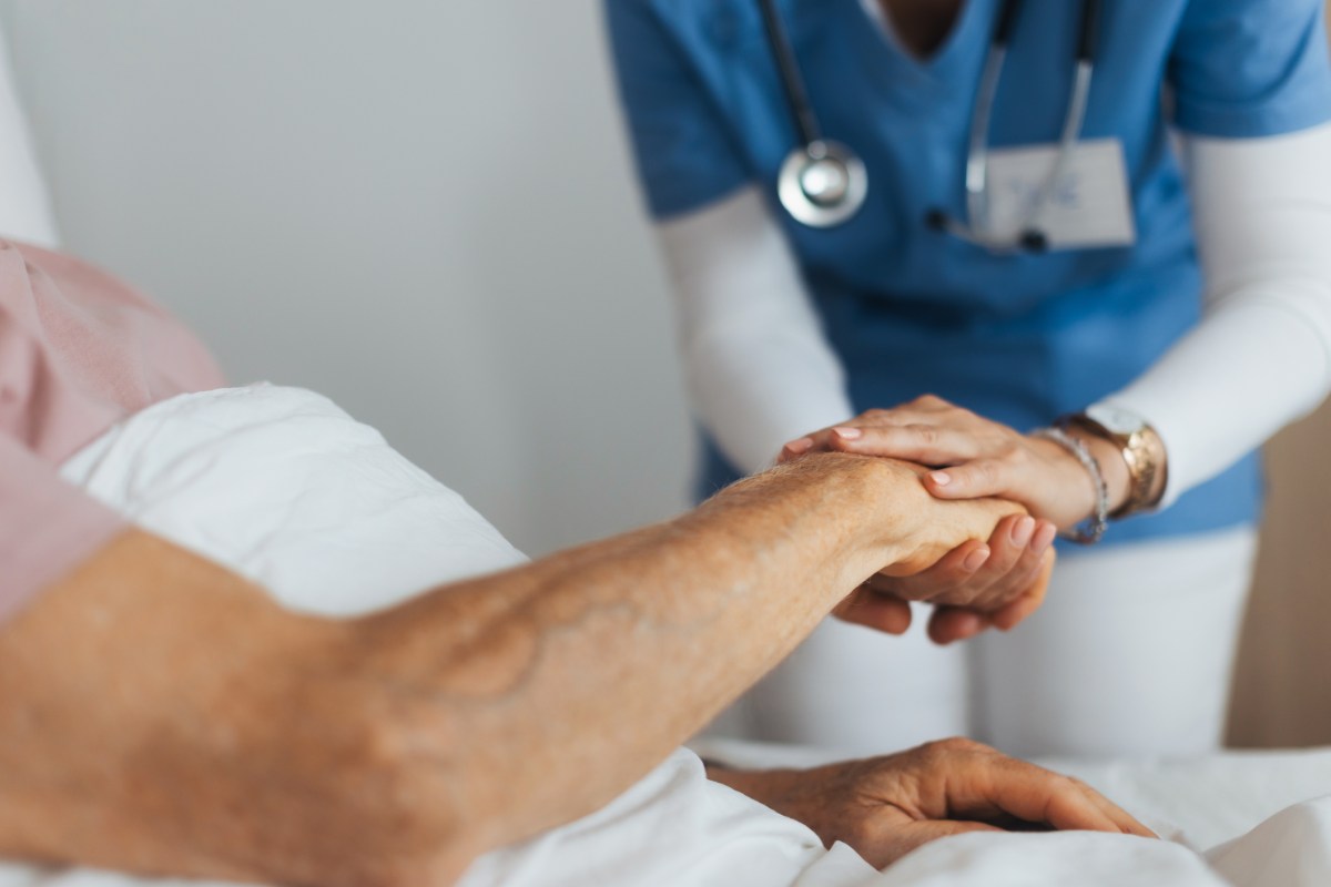 Close-up of caregiver holding senior client hand. Support from nurse to patient, taking care of elderly man in hospital. Emotional support and care in healthcare, hospice care.