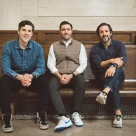 three men who own Zaro's Family Bakery sitting on a bench in a train station