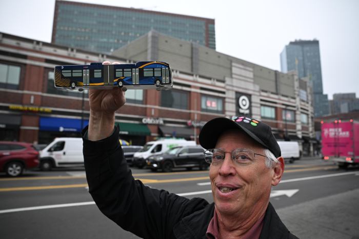 man holding up a small model bus on a street in Brooklyn