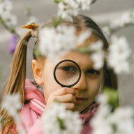 Kid learning about environment. Natural education activity for World Earth day. Exploring in spring, blooming flowers in the garden. Serious girl looking though the magnifying glass