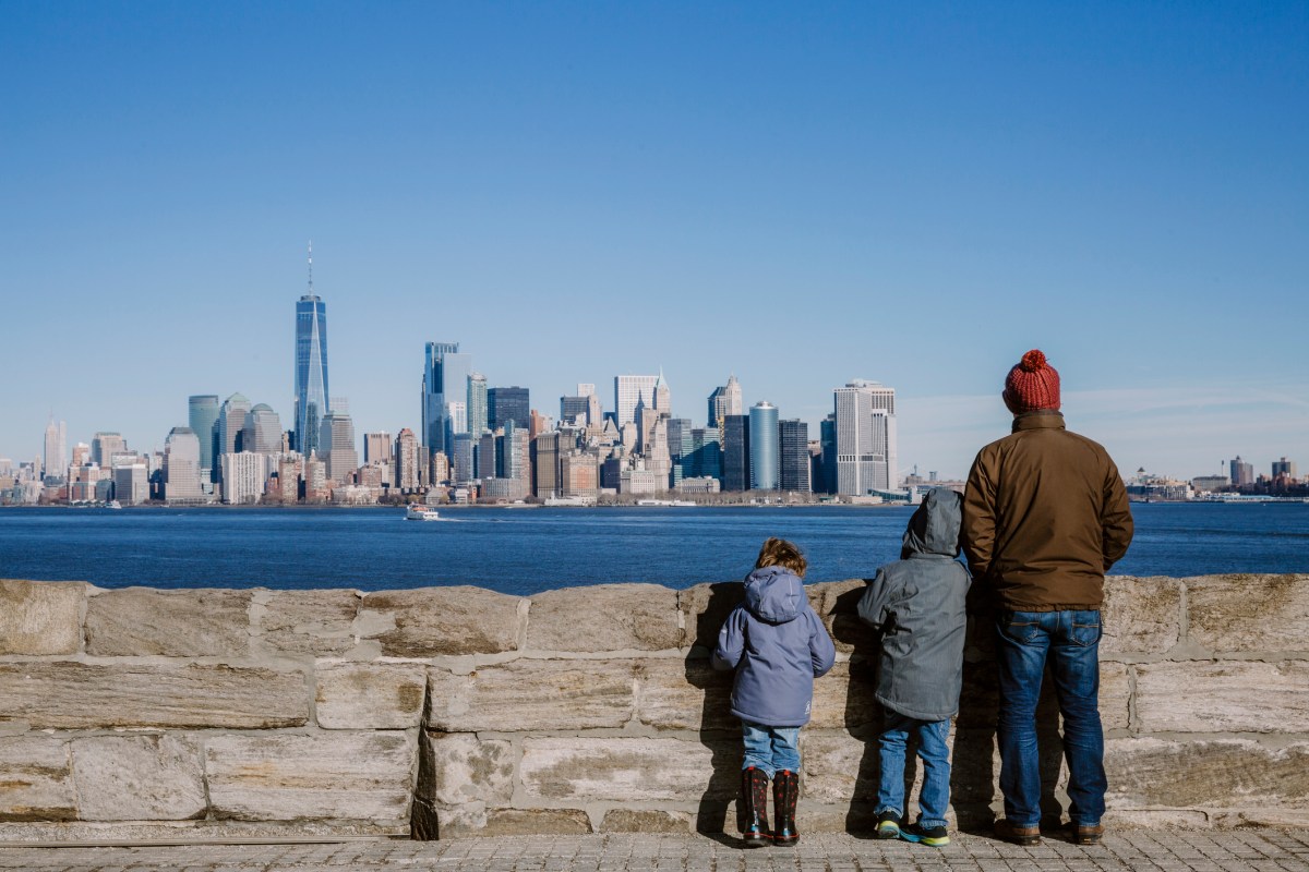 Rear view of father and sons wearing warm clothing looking at cityscape by river against sky