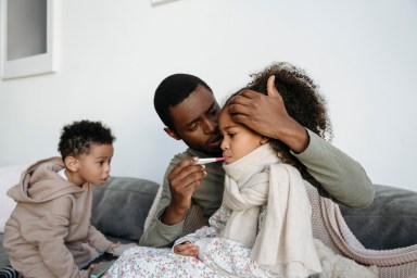 Caring father with thermometer checking fever of daughter by son