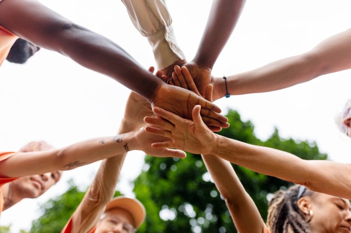 Directly below shot of multiracial volunteers stacking hands during environmental cleanup program. Multiethnic men and women cheering before cleaning the city park.