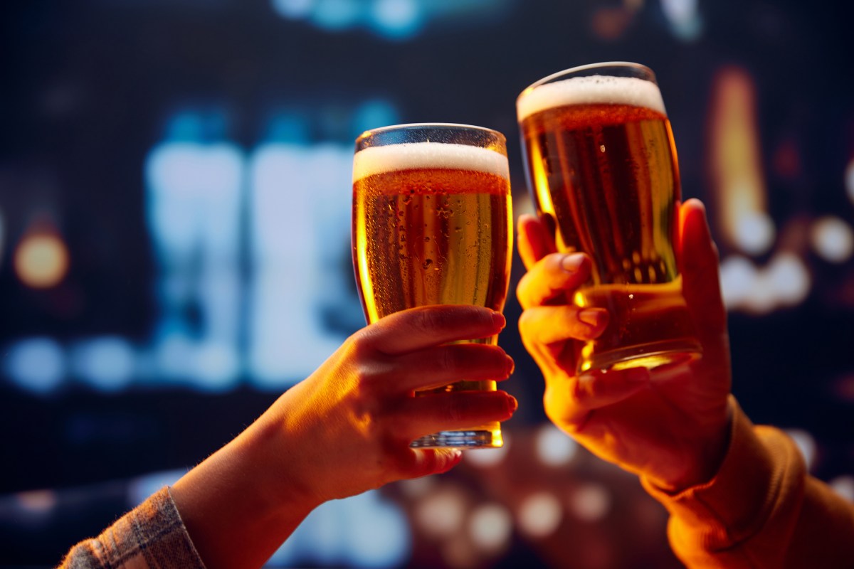 Hands holding lager light foamy big beer glasses and clinking. Two friends sitting in bar and drinking alcohol drinks. Concept of Beer Fest, party, celebration, taste, national traditions.