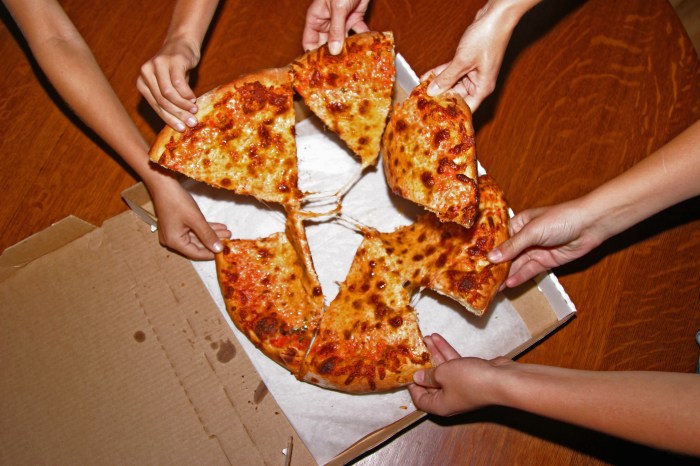 People grabbing slices of pizza, overhead view