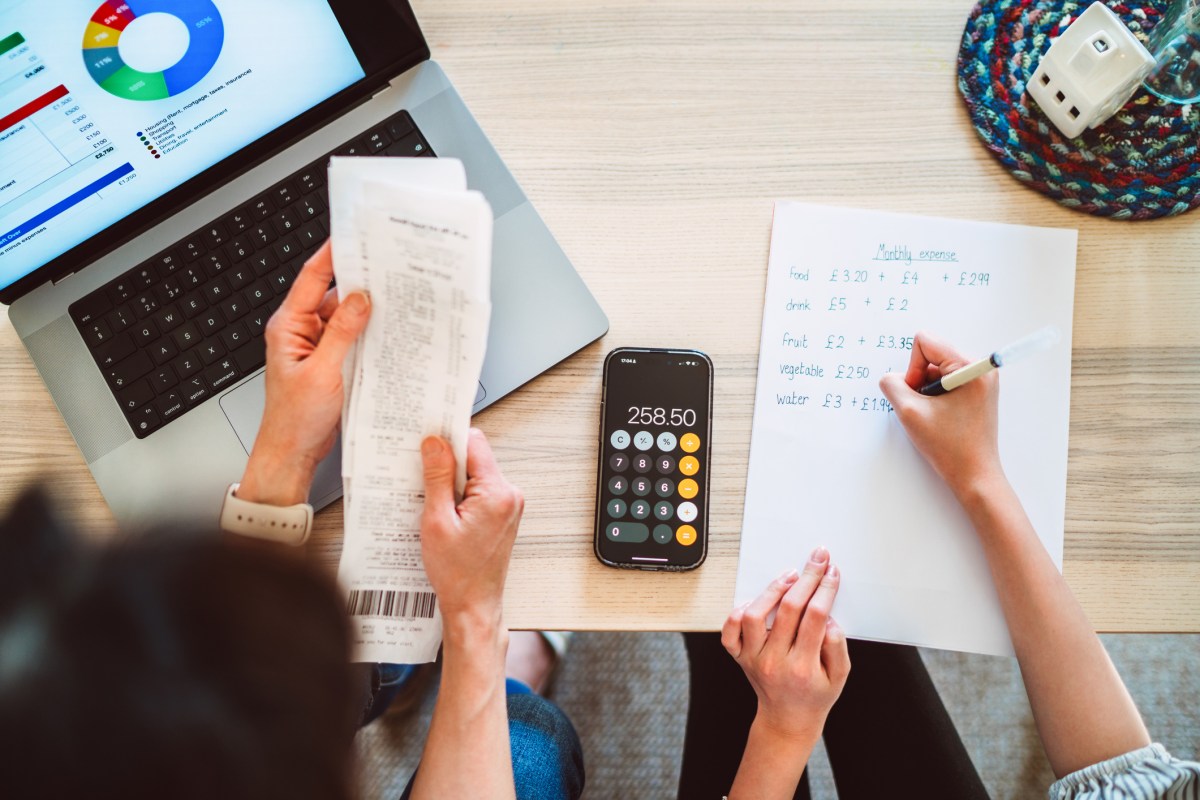 A direct above and personal perspective shot of a young mother and her teenage daughter working together to manage their household budget. The mother and the daughter is preparing home expenses data for information input to the A.I. financial app. With a laptop displaying a AI.I generated pie chart of expenses sits on the table, illustrating their thorough approach to financial planning. This image emphasises the importance of financial literacy, teamwork, and practical education at home. Concept of budgeting, financial education, home management, and integration of A.I. tools into daily life.