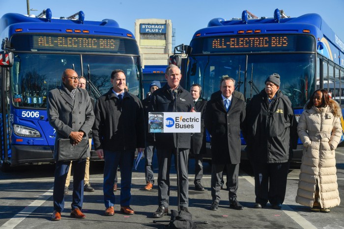 people talking in NYC in front of two electric buses during the day