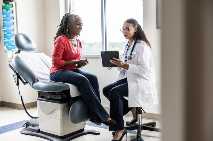 Female doctor and senior woman looking at digital tablet in exam room