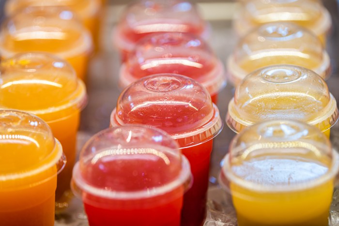 Closeup of many red yellow juice drink cocktail plastic cups beverages and cover in shop store counter in summer