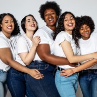 Group of females standing on white background and laughing. Multi-ethnic women in white t-shirt and blue jeans hugging each other.