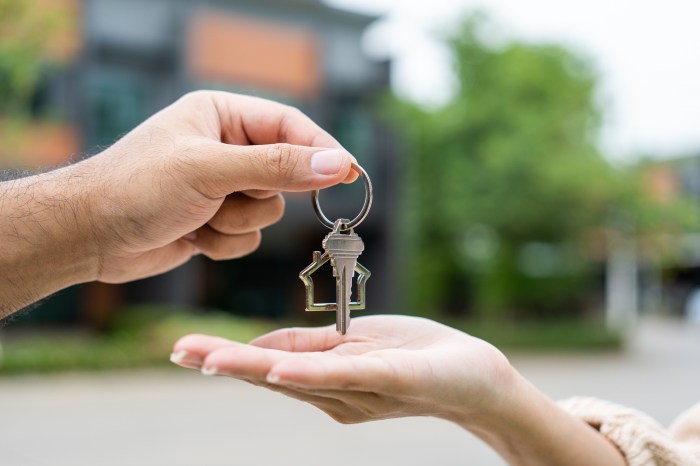 Woman buying or rent new home she holding key front of new house. Surprise happy young asian woman giving house key and smile to rent or purchase apartment home. Moving relocation concept.