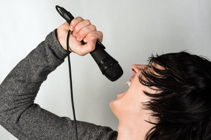 The young black hair guy is singing or screaming in the microphone on gray background.